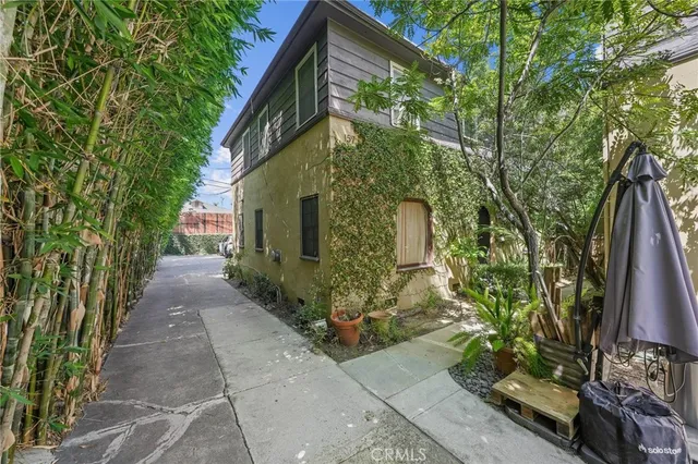 a pathway of a house with potted plants and large trees
