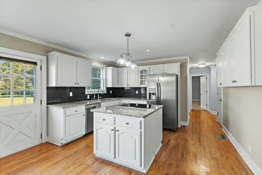 a kitchen with stainless steel appliances granite countertop a refrigerator a stove a sink dishwasher and white cabinets with wooden floor