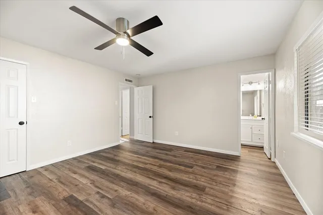 an empty room with wooden floor ceiling fan and windows