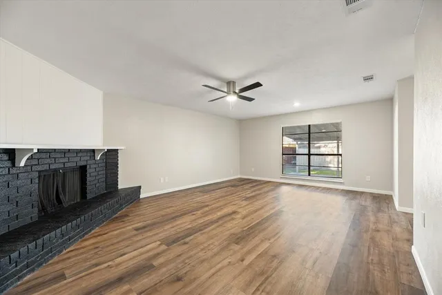 an empty room with wooden floor fireplace and windows