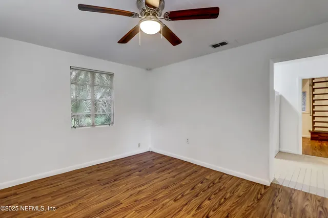 an empty room with wooden floor chandelier fan and windows