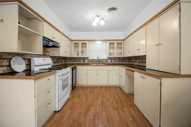 a white kitchen with wooden floor and stainless steel appliances