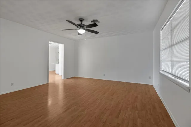an empty room with wooden floor fan and windows