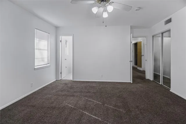 an empty room with chandelier fan and windows