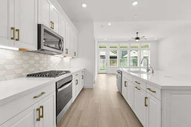 a large white kitchen with stainless steel appliances granite countertop a stove and a sink