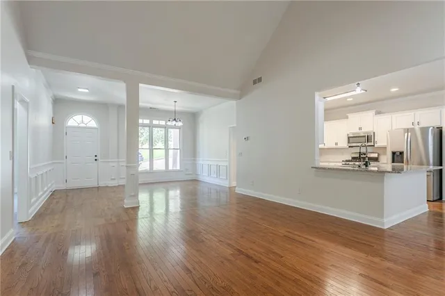 a view of an empty room with wooden floor and a kitchen