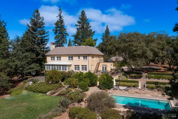 a view of a white house with a yard plants and large tree