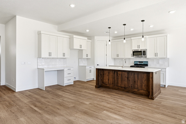 4978 North 75 East Enoch, UT 84721 - Photo 5 of 60 Two tone kitchen with backsplash, stainless steel appliances, a kitchen island with sink, light wood-type flooring, and dual tone cabinetry