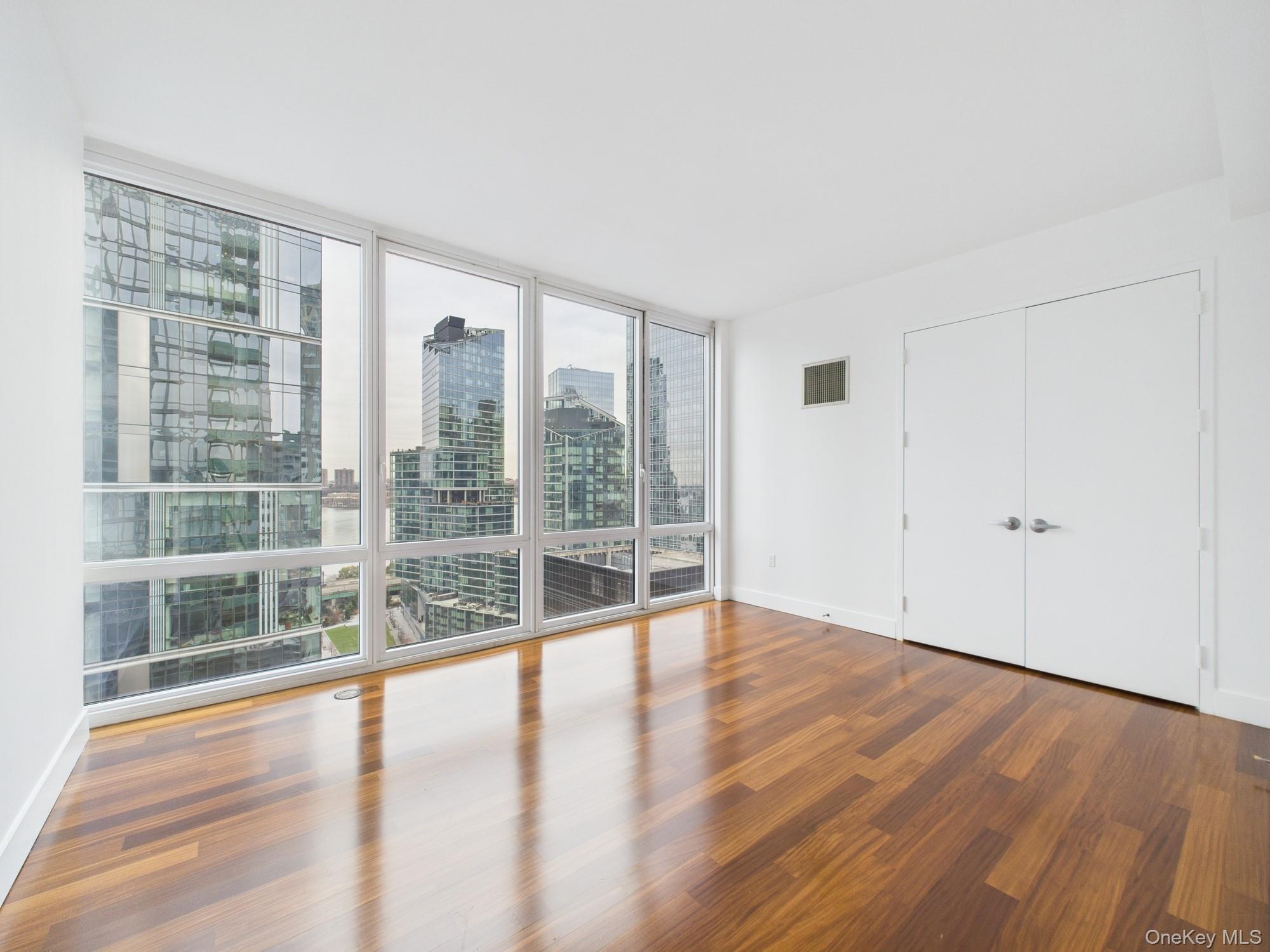 10 West End Avenue, Unit 20B Manhattan, NY 10023 - Photo 24 of 41 Unfurnished bedroom with expansive windows, wood finished floors, a view of city, and a closet