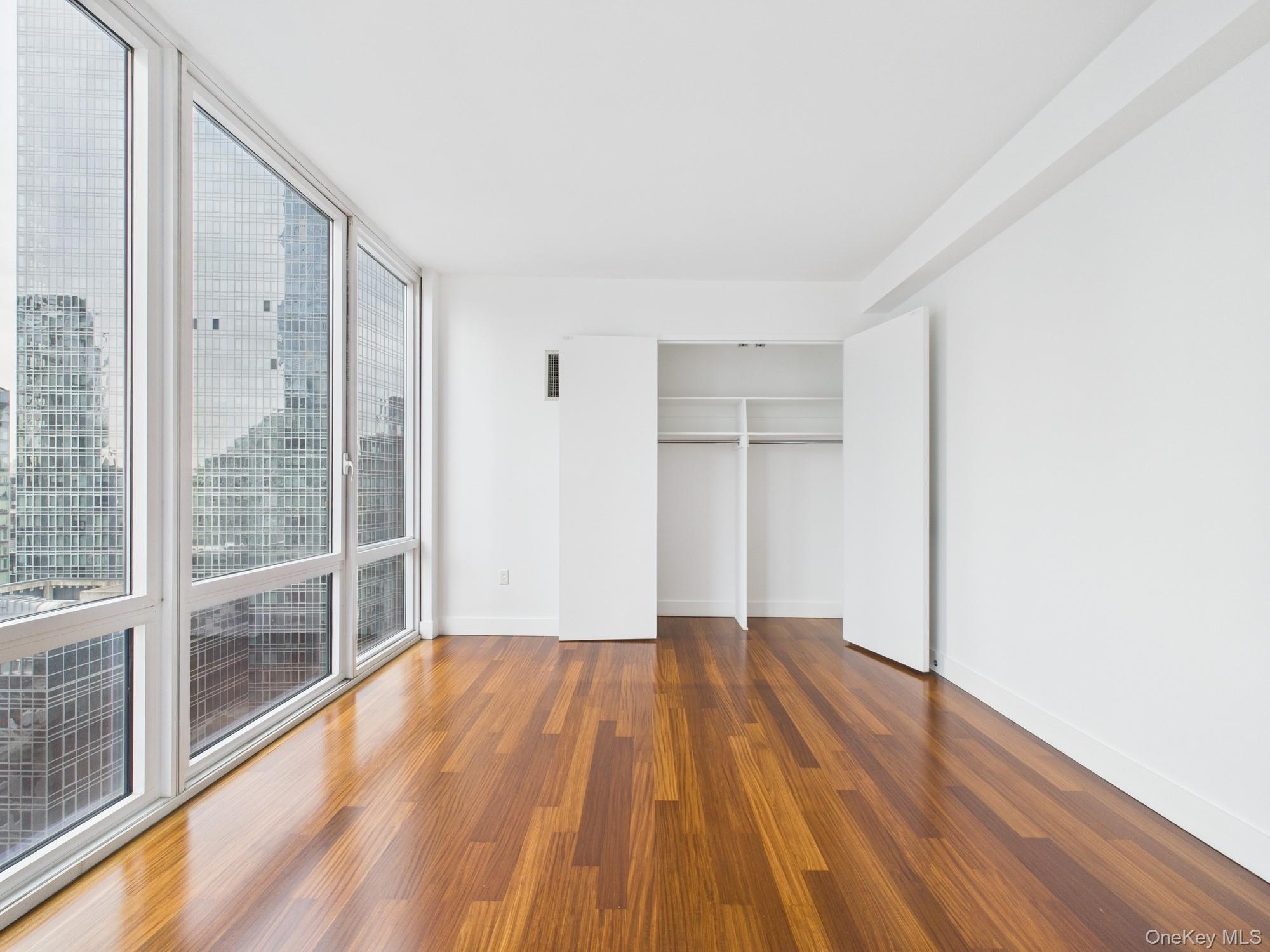 10 West End Avenue, Unit 20B Manhattan, NY 10023 - Photo 26 of 41 Unfurnished bedroom with a wall of windows, wood finished floors, and a closet