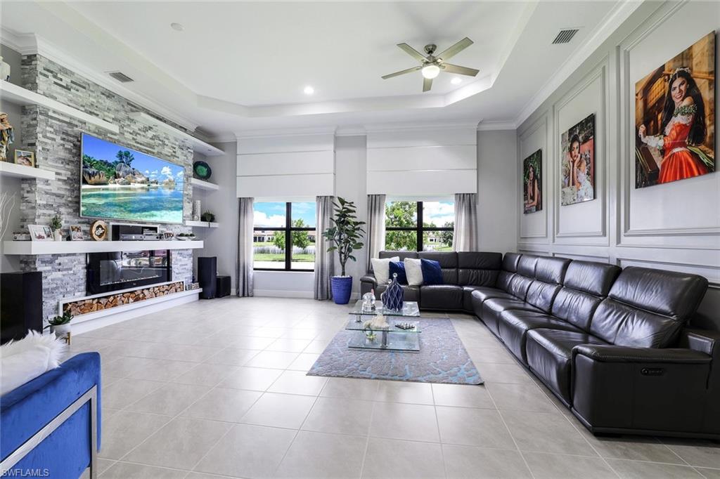 4795 Rosetta Terrace Immokalee, FL 34142 - Photo 3 of 27 Living room with built in features, a fireplace, a ceiling fan, light tile patterned floors, and crown molding