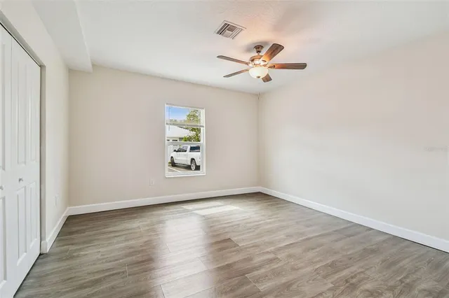 an empty room with wooden floor fan and windows