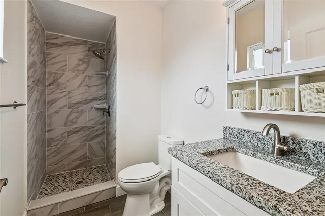 a bathroom with a granite countertop sink a toilet a mirror and shower