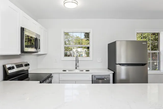 a kitchen with stainless steel appliances a refrigerator a sink a stove and white cabinets