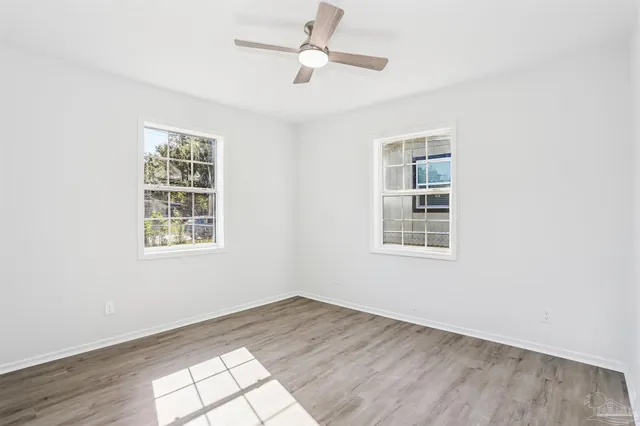 an empty room with wooden floor ceiling fan and windows