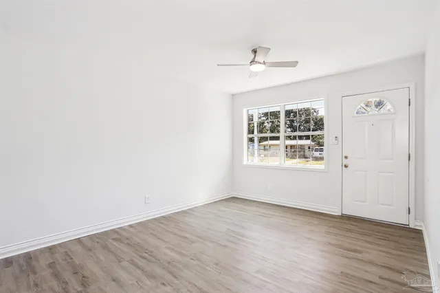 an empty room with wooden floor chandelier fan and windows