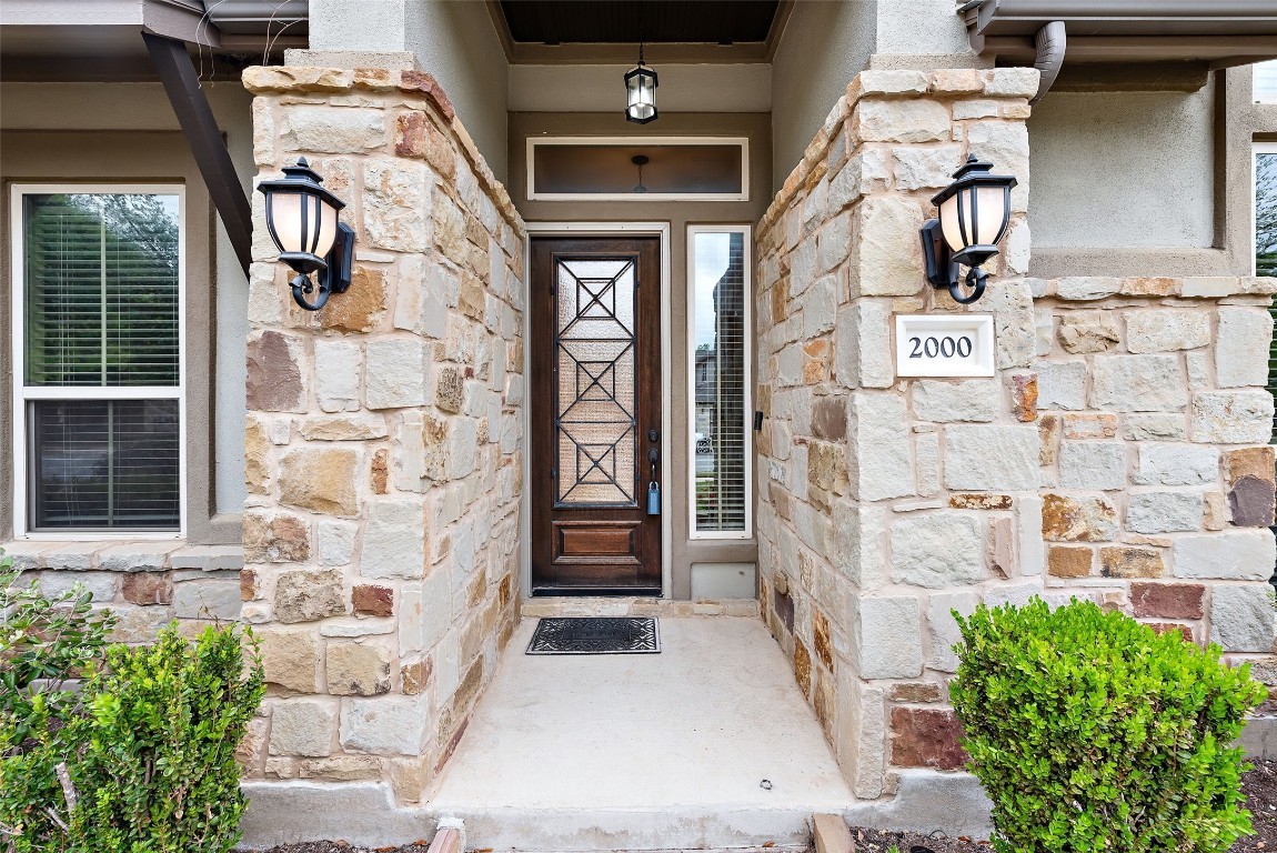 2000 Manada Trail Leander, TX 78641 - Photo 4 of 36 Stone facade entrance featuring a richly stained wood door and elegant outdoor lighting.