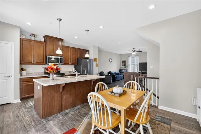 a kitchen with stainless steel appliances a dining table chairs a microwave oven and a refrigerator with wooden floor