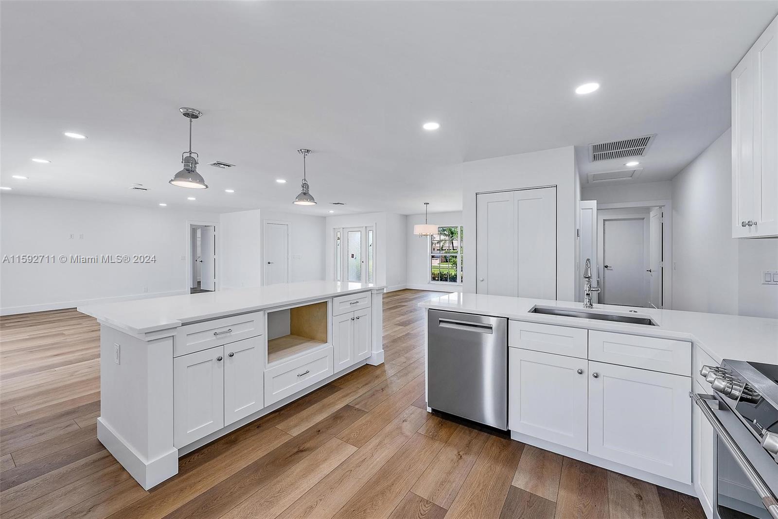 8547 Southeast Merritt Way Jupiter, FL 33458 - Photo 7 of 27 a large white kitchen with a large island oven a sink dishwasher and white cabinets with wooden floor