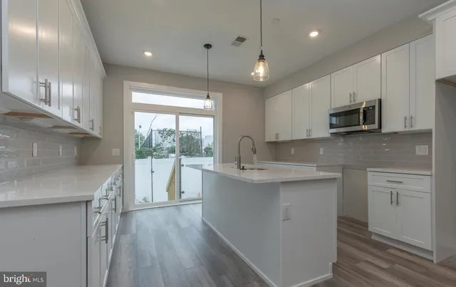 a kitchen with kitchen island granite countertop a stove a sink a refrigerator and white cabinets with wooden floor