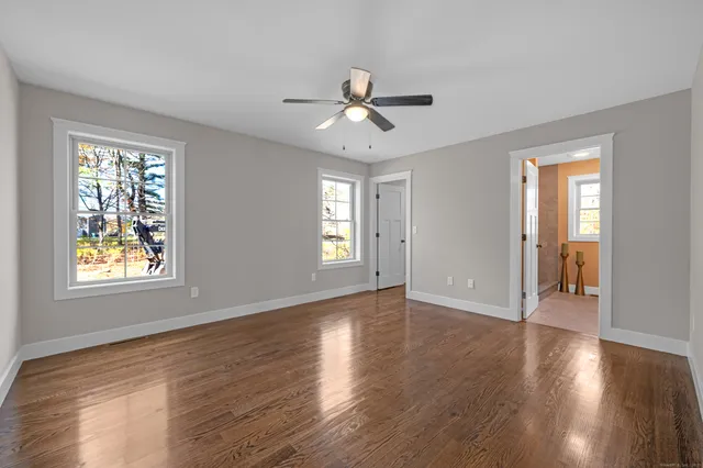 a view of an empty room with wooden floor and a ceiling fan
