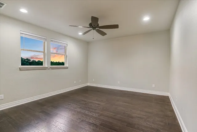 an empty room with wooden floor fan and windows