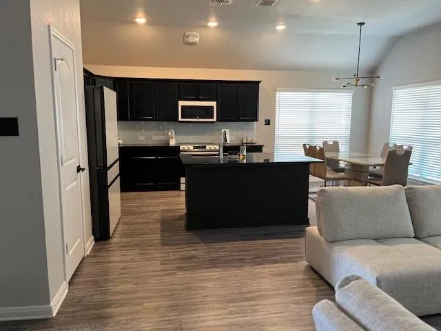 a living room with stainless steel appliances kitchen island granite countertop a refrigerator a stove top oven a sink and dishwasher with wooden floor