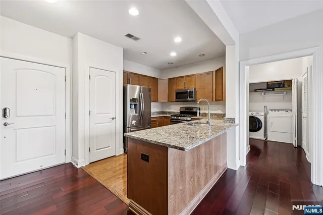 a kitchen with stainless steel appliances granite countertop a refrigerator a sink dishwasher a stove and a oven with wooden floor