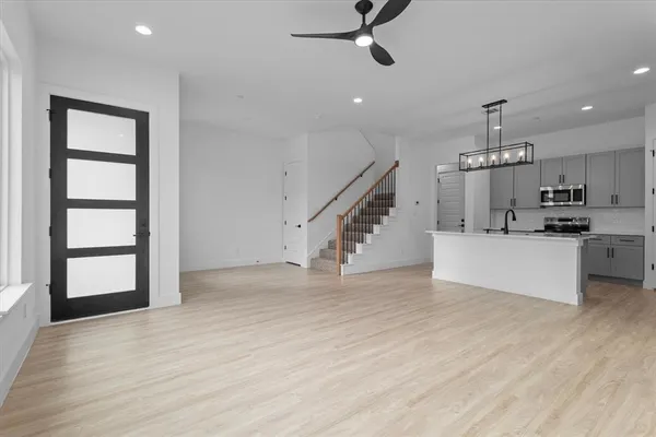 an empty room with wooden floor staircase and kitchen view