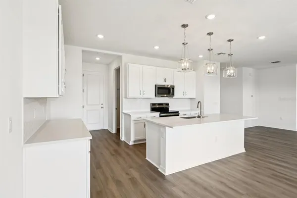 a kitchen with stainless steel appliances a stove top oven a refrigerator a sink and white cabinets with wooden floor