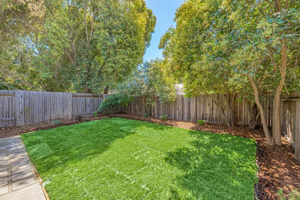 a backyard of a house with table and chairs plants and large tree