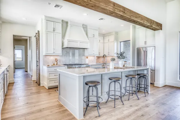 a kitchen with stainless steel appliances granite countertop a refrigerator a sink dishwasher a stove and white cabinets with wooden floor