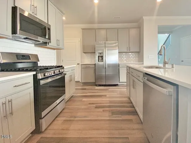 a kitchen with stainless steel appliances granite countertop a stove top oven a sink dishwasher a refrigerator and a microwave oven with large wooden cabinets