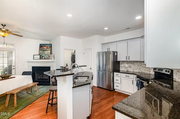 a kitchen with stainless steel appliances granite countertop a stove top oven a sink dishwasher a refrigerator and white cabinets with wooden floor