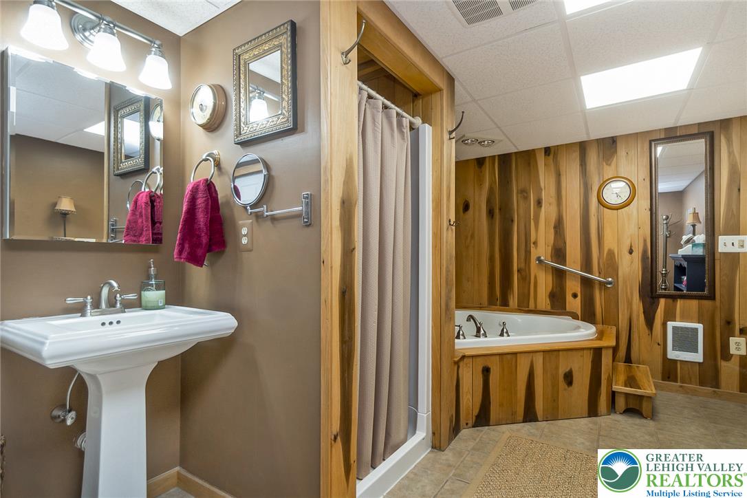 540 Briar Road Pen Argyl, PA 18072 - Photo 60 of 66 A comfortable bathroom featuring a classic pedestal sink and a deep soaking tub surrounded by natural wood paneling.