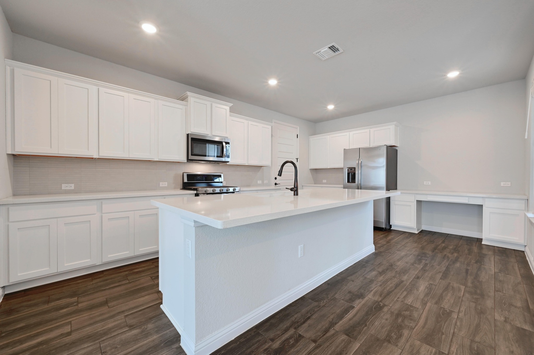 8003 Orizzonte Street Austin, TX 78744 - Photo 11 of 25 Kitchen featuring stainless steel appliances, white cabinets, dark wood-style floors, a center island with sink, and recessed lighting