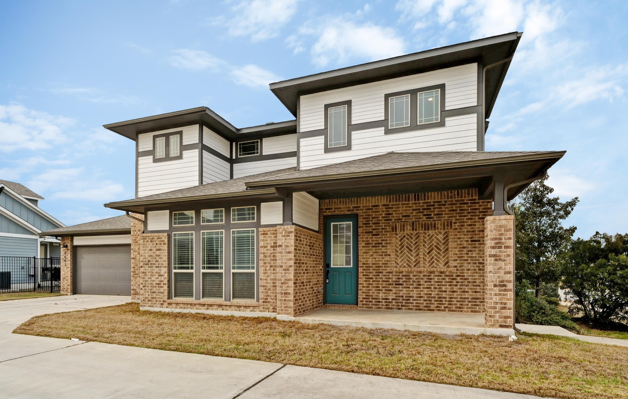 8003 Orizzonte Street Austin, TX 78744 - Photo 2 of 25 Prairie-style home featuring brick siding, a porch, driveway, and an attached garage