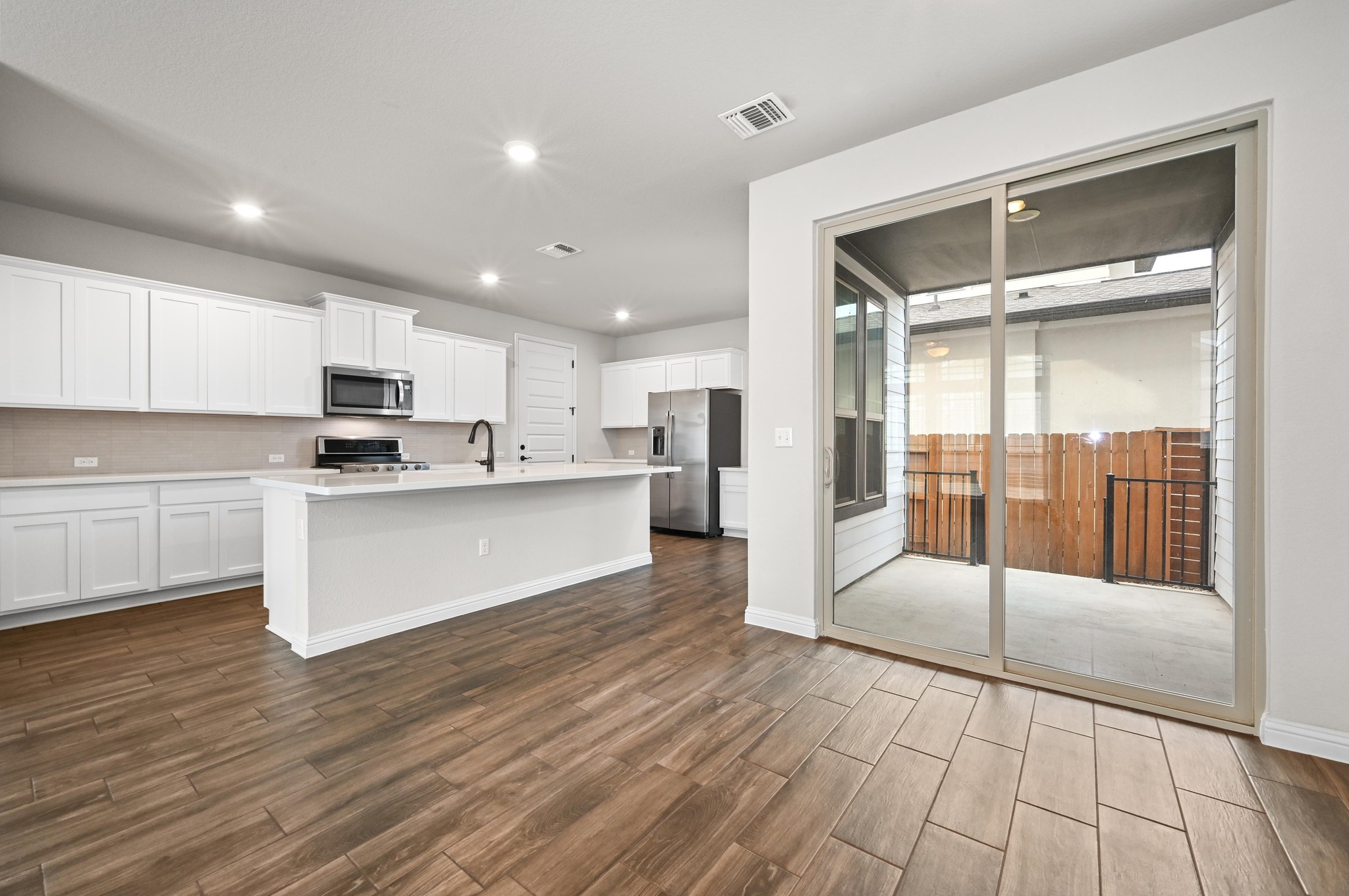 8003 Orizzonte Street Austin, TX 78744 - Photo 10 of 25 Kitchen with white cabinetry, wood tiled floors, stainless steel appliances, a center island with sink, and recessed lighting