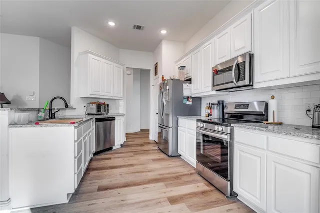 a kitchen with stainless steel appliances granite countertop a stove top oven a sink dishwasher and a refrigerator with wooden floor