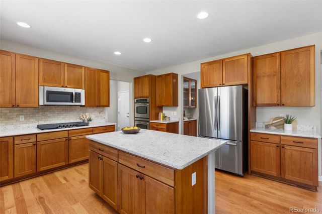 a kitchen with stainless steel appliances granite countertop a refrigerator a sink dishwasher a stove with wooden cabinets and wooden floor