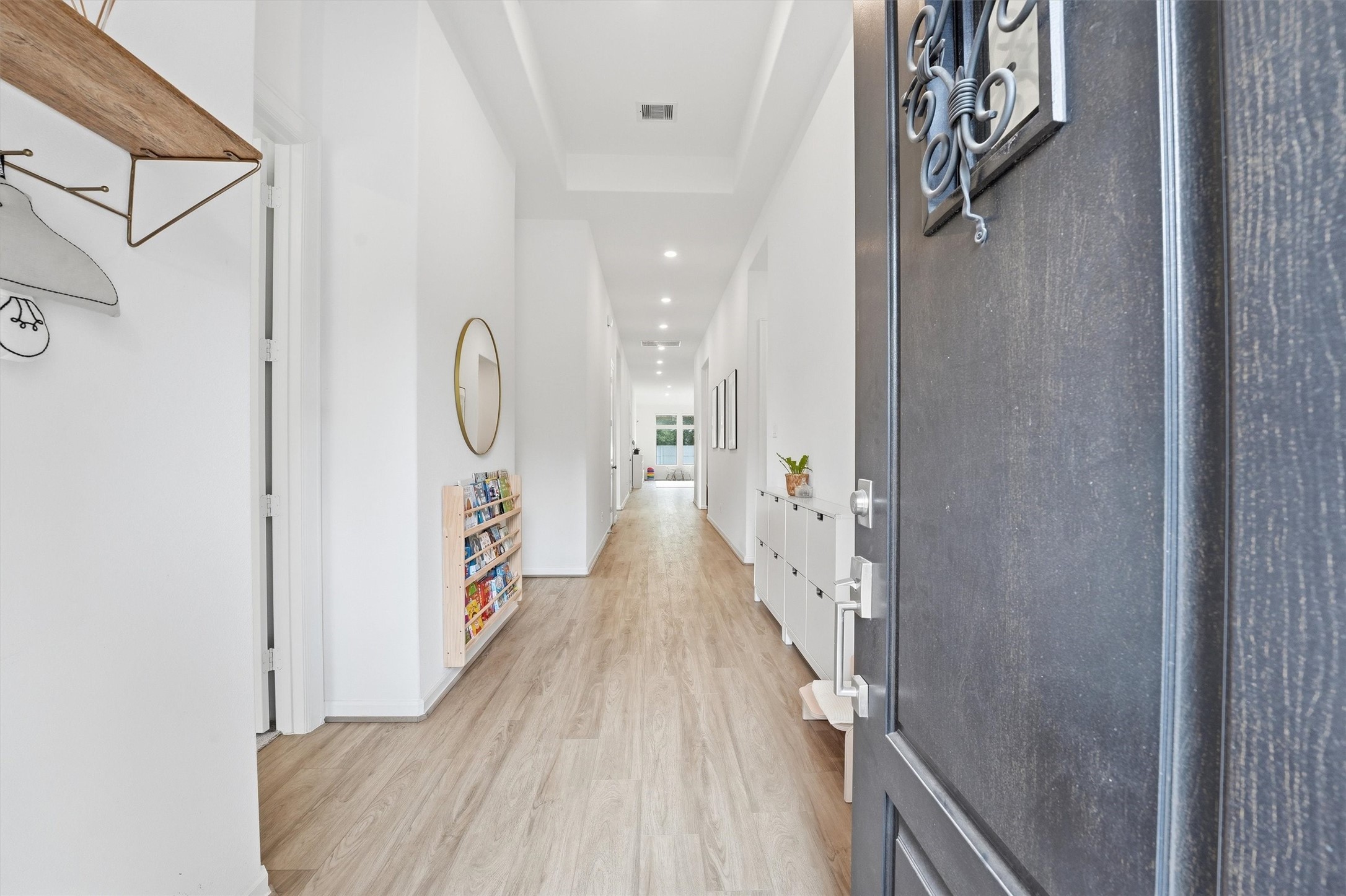 6071 Windward Falls Way Porter, TX 77365 - Photo 3 of 33 This photo showcases a bright, long hallway with wood flooring, white walls, and modern decor. Recessed lighting enhances the contemporary feel. The space leads to an inviting open area visible at the end.