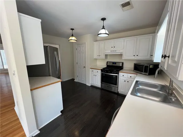 a kitchen with granite countertop a refrigerator a sink dishwasher a stove and white cabinets with wooden floor