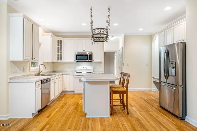 a kitchen with stainless steel appliances a refrigerator a stove a sink dishwasher a dining table and chairs with wooden floor