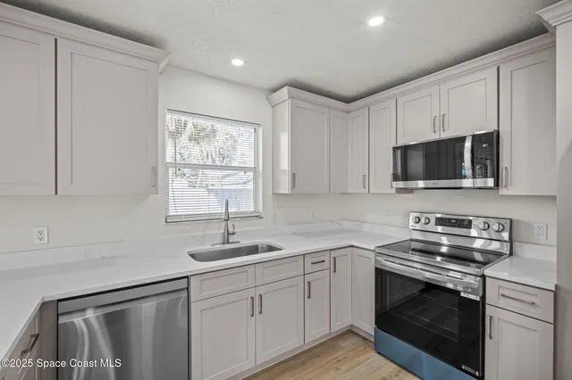 a kitchen with granite countertop white cabinets appliances a sink and a window