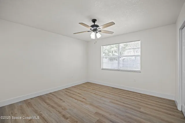 an empty room with wooden floor fan and windows