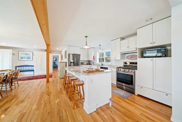 a kitchen with stainless steel appliances a stove top oven a sink a refrigerator white cabinets and wooden floor