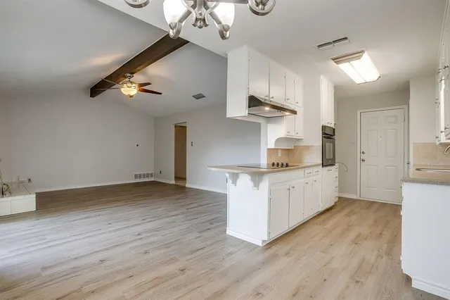 a kitchen with stainless steel appliances granite countertop a sink dishwasher a stove a refrigerator and white cabinets with wooden floor