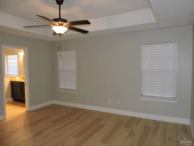 an empty room with wooden floor chandelier fan and windows