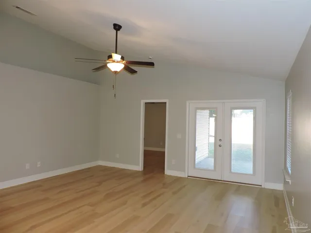 a view of an empty room with chandelier fan and wooden floor