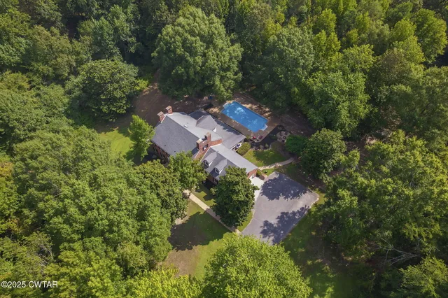 an aerial view of a house with outdoor space and trees all around